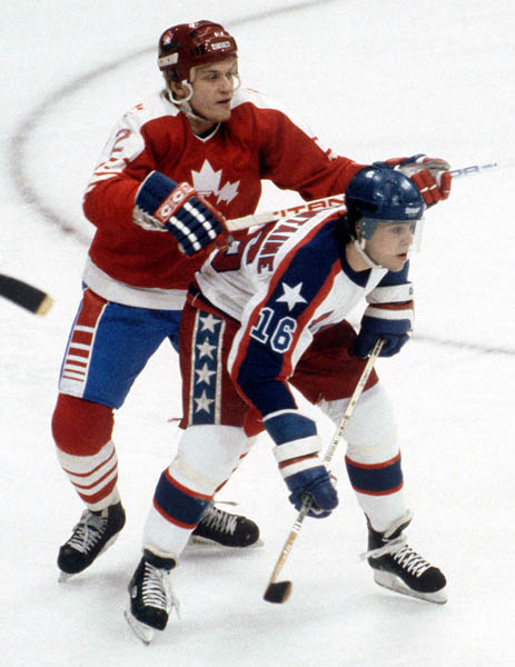 Robin Bartel (2) du Canada pose un double-chec sur Patrick LaFontaine au hockey contre les tats-Unis aux Jeux olympiques d'hiver de Sarajevo de 1984. (Photo PC/AOC)
