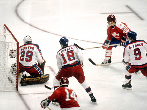 Team Canada's Carey Wilson takes a shot on goal as United States' Al Iafrate (18) and Scott Fusco (9) of come in to help their goalie during hockey action at the 1984 Winter Olympics in Sarajevo. (CP PHOTO/ COA/O. Bierwagon )