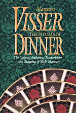 Cover of cookbook, THE RITUALS OF DINNER: THE ORIGINS, EVOLUTION, ECCENTRICITIES, AND MEANING OF TABLE MANNERS, with a photograph of a green brocade tablecloth and four gold-edged patterned china plates