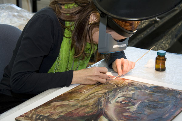 A conservator leaning over a painting holding a cleaning swab