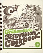 Cover of cookbook, GRAHAM KERR'S TELEVISION COOKBOOK, with a caricature-style drawing of a man, probably Graham Kerr, carrying a tray of food while a woman hugs him