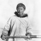 Photograph of Memogana, an Inuit interpreter for the RCMP, who is standing on a dock and holding a telescope, [Fullerton], Nunavut, circa 1904-1905